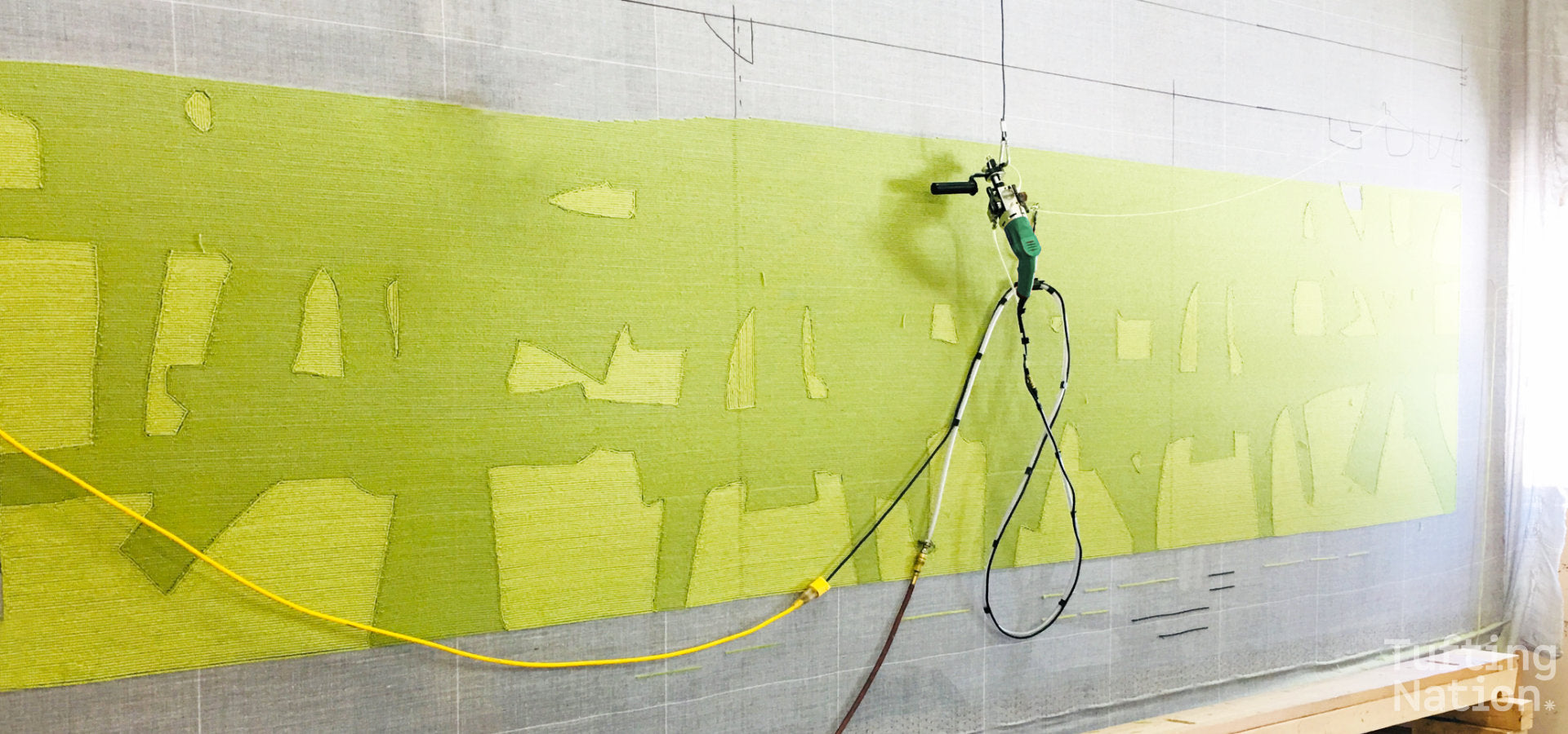 Green Tufting Gun making a large tufted rug stretched over a huge tufting frame | TuftingNation