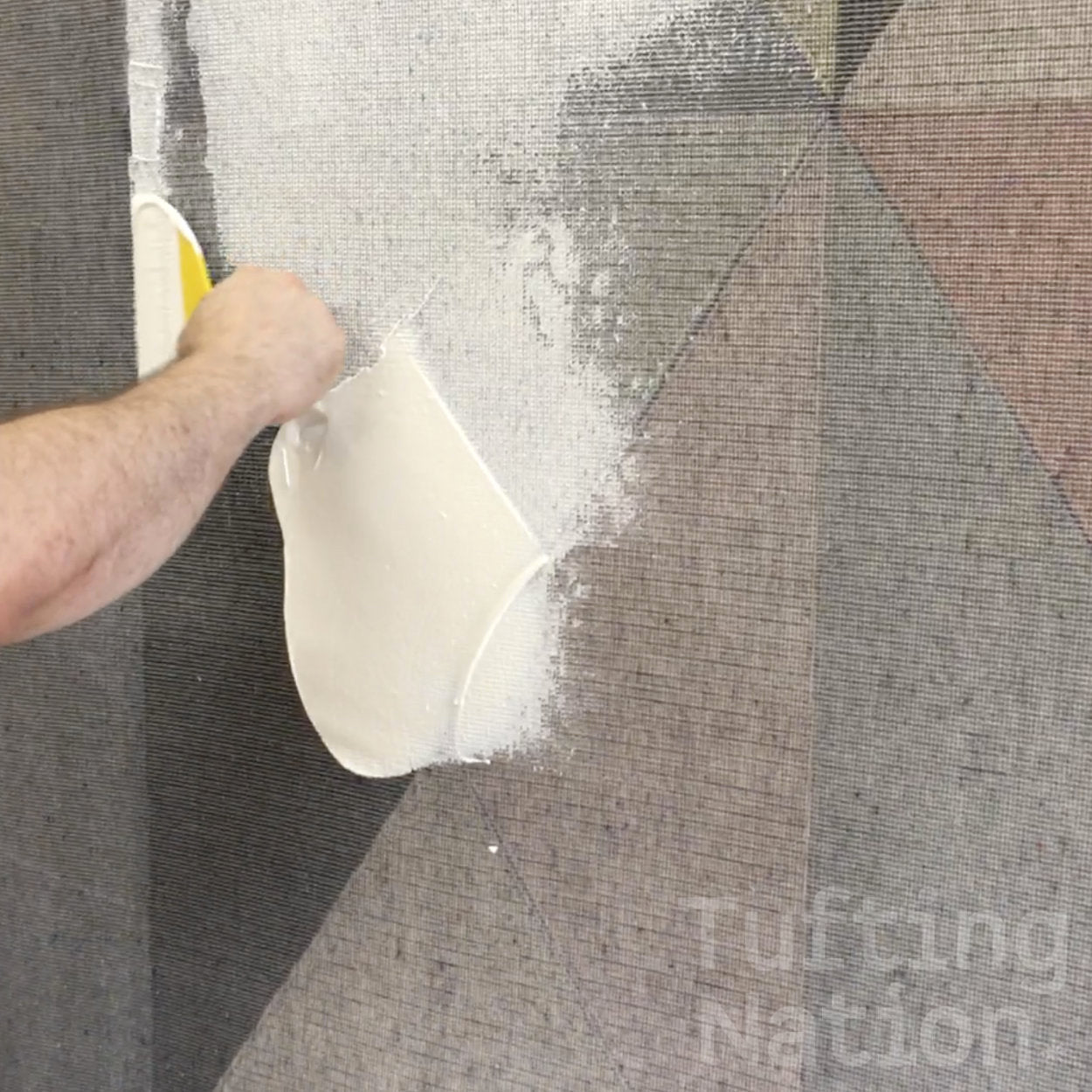 TN-200 Rug Adhesive being applied to the back of a hand tufted rug over a secondary rug backing | TuftingNation